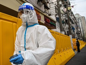 A worker, wearing a protective gear, walks next to tbarriers that separate from the street an neighbourhood in lockdown as a measure against COVID-19 in Jing'an district, in Shanghai on March 30, 2022.