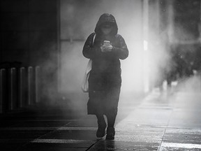 A masked pedestrian walks down Toronto’s Bay Street surrounded by steam on Tuesday March 15, 2022.