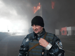 A Ukrainian soldier walks by as fire and smoke rise over a building following shelling in Kyiv, Ukraine, Thursday, March 3, 2022.