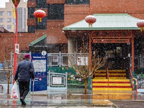 A pedestrian crosses a street in Calgary’s Chinatown as flurries fall on Tuesday, April 19, 2022.
