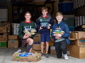 Grade 8 student Kate Bishop, left, her brother Luc, 9, and grade 8 student Alexander Bilson pose for a portrait with the donated pasta they have gathered to send to Ukrainian refugees in Ukraine and Poland on Monday, April 25, 2022.
