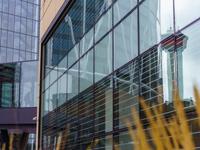 The Calgary Tower is reflected on an office building as a downtown office worker crosses a Plus-15 on a chilly day in Calgary on Wednesday, April 13, 2022.