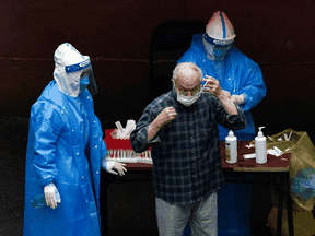 Workers in protective suits are seen Tuesday in Shanghai working with a man at a nucleic acid testing site during a strict lockdown brought about by the COVID-19 pandemic.