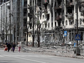 FILE PHOTO: People walk along a street near a building damaged during the Ukraine-Russia conflict in the southern port city of Mariupol, Ukraine on April 25, 2022.