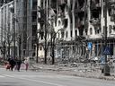 FILE PHOTO: People walk along a street near a building damaged during the Ukraine-Russia conflict in the southern port city of Mariupol, Ukraine, on April 25, 2022. 