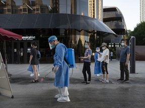 A health worker sprays disinfectant as people wait to get a COVID-19 test on May 25, 2022, in Beijing, China.