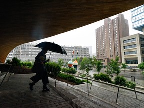 FILE - A person walking out of the Central Library takes shelter under an umbrella while rain pours in Calgary on Monday, June 13, 2022.