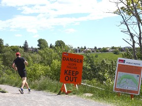 A runner takes a pathway near signs warning residents and pathway users of possible dangers at the top of McHugh Bluff on Crescent Rd NW in Calgary on Wednesday, June 22, 2022.