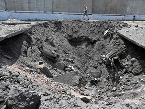 A man walks past a huge crater created by the impact of a Russian rocket in an industrial zone in Kharkiv on June 30, 2022.