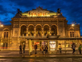 People wait for a tram in front of the lit-up Wiener Staatsoper, Vienna's State Opera house, during the twilight in the city centre on Aug. 12, 2014.