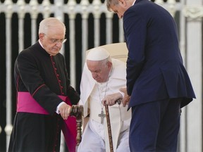 Pope Francis is helped to stand up by his aide Monsignor Leonardo Sapienza, left, at the end of the weekly general audience in St. Peter's Square at The Vatican, Wednesday, June 8, 2022.