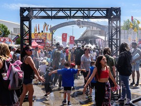 People cool off under the arch of fog in the middle of Stampede Park on the first day of the Calgary Stampede on Friday, July 8, 2022.
