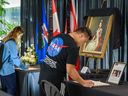 Chenaniah Malay, a la izquierda, y Branzh Riveral escriben en libros de condolencias en honor a la difunta reina Isabel II en el ayuntamiento de Calgary el martes.