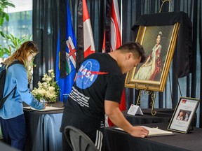 Chenaniah Malay, left, and Branzh Riveral write in condolence books honouring the late Queen Elizabeth II at Calgary city hall on Tuesday.