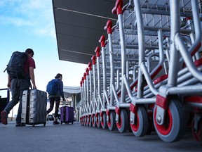 Passengers walk past baggage carts on their way to Calgary International Airport on Monday.