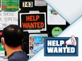 A pedestrian passes a "Help Wanted" sign in the door of a hardware store.