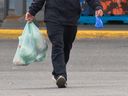 A shopper leaves a store in Sunridge with groceries in plastic bags in Calgary.