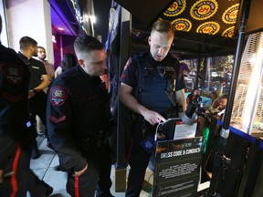 Members of the Calgary Police Violent Crime Suppression Team (formerly the Gang Suppression Unit) view customer data on an electronic device outside a popular nightclub on 16 Ave SW in downtown Calgary on June 18, 2022. Police say that the men and women they keep an eye on visit all kinds of venues - from high end restaurants, strip clubs, nightclubs, pubs and popular restaurants in all areas in and around Calgary.