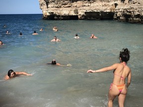 Italians cavorting at Lama Monachile, a famous cove and beach in Polignano a Mare. One time use photo only by Alex Berenyi.