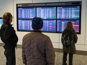 Travelers look at a flight status board at Calgary International Airport on Tuesday, Dec. 20, 2022. Weather issues across Canada have caused flight delays and cancellations.