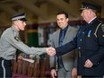 Will Fossen, deputy chief with transit public safety, emergency management and community safety, centre, and Aaron Coon, public vehicle standards chief, hand badges and certificates to 13 new transit peace officers at a graduation ceremony at Mewata Armoury on Friday.