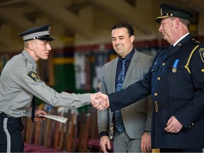 Will Fossen, deputy chief of public transportation safety, emergency management and community safety, center, and Aaron Coon, chief of public vehicle standards, present badges and certificates to 13 new transit peace officers at a graduation ceremony at Mewata Armory on Friday.