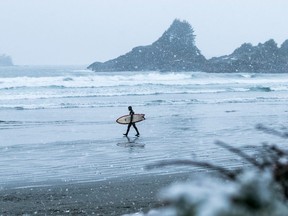 Surfer walking on the beach towards the ocean in the snow at Cox Bay, Tofino. Courtesy, Destination BC/Keenan Bush