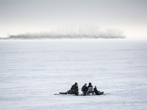 Ice fishermen huddle over a hole in the ice on Ghost Lake Reservoir near Cochrane, Alta., Sunday, Dec. 27, 2020. Alberta's United Conservative government has moved on a plan to split the job of wildlife management in the province, creating a new department of hunting and fishing in the Forestry, Parks and Tourism Ministry.