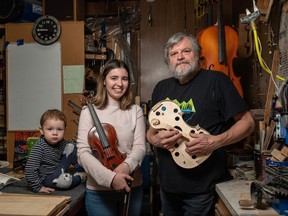 Ukrainian violinist Anastasiia Lykhosherstova and her two-year-old son Elisha, pose for a photo with luthier Ross Hill and the violin he has gifted to Lykhosherstova at his shop in Calgary.