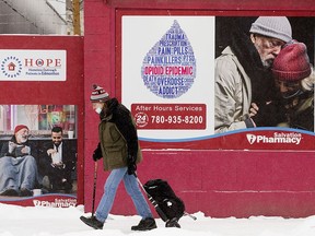 A pedestrian makes their way past an opioid epidemic poster on the side of Salvation iPharmacy, 10570 96 St., in Edmonton on Dec. 16, 2021.