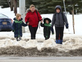 Ashley Price scales a windrow as she crosses a marked crosswalk with her two sons, aged 4 and 6, and a family friend on Old Banff Coach Rd SW on Friday, March 3.