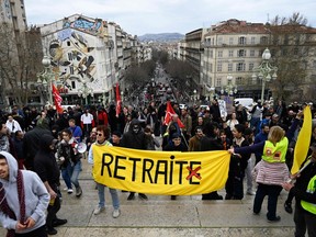 Protesters hold a yellow banner which reads "Pension", with a crossed 'E' at the end of the word - retraite -, which means in French "removal", during a demonstration, on the stairs outside the Gare Saint-Charles train station in Marseille, southern France, on March 18, 2023, two days after the French government pushed a pensions reform through parliament without a vote, using the article 49.3 of the constitution. - France on March 18 braced for a weekend of protests, after a second night of unrest sparked by the French president imposing without a parliament vote an unpopular pension overhaul, that includes raising the retirement age from 62 to 64.