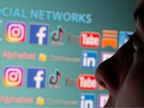 A woman is seen in front of displayed social media logos in a photo illustration.