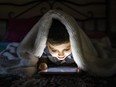 Little child using a tablet covered with a blanket