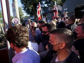 A man, top right, throws gravel at Liberal leader Justin Trudeau, left, as the RCMP security detail provide protection, while protesters shout at a local microbrewery during the Canadian federal election campaign in London Ont., on Monday, September 6, 2021. The Ontario man who threw gravel at Trudeau during a 2021 federal election campaign event marred by protest is set to be sentenced today.