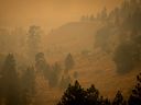 Smoke from wildfires fills the air as motorists travel on a road on the side of a mountain, in Kelowna, B.C., on Saturday.