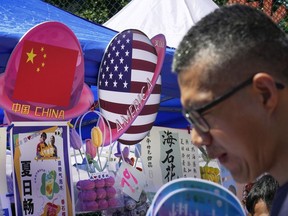 FILE - A man walks by a booth selling foods and beverages displaying planet-shaped flags of China and the U.S. during a spring carnival in Beijing on May 13, 2023. China has detained a worker from a military industrial group on suspicion of spying for the CIA, national security authorities said Friday, Aug. 11, 2023, adding to the list of public accusations of espionage between Beijing and Washington.