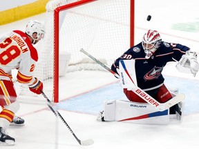 Columbus Blue Jackets goalie Spencer Martin, right, stops a shot by Calgary Flames forward Elias Lindholm, left, during the third period of an NHL hockey game in Columbus, Ohio, Friday, Oct. 20, 2023.
