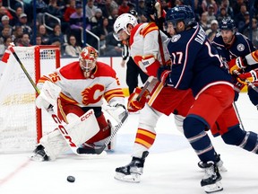 Calgary Flames goalie Jacob Markstrom, left, makes a stop in front of Flames defenseman Chris Tanev, center, and Columbus Blue Jackets forward Justin Danforth during the second period of an NHL hockey game in Columbus, Ohio, Friday, Oct. 20, 2023.