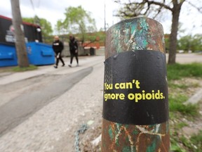 Pedestrians walk past a sticker raising awareness about opioids in Edmonton.