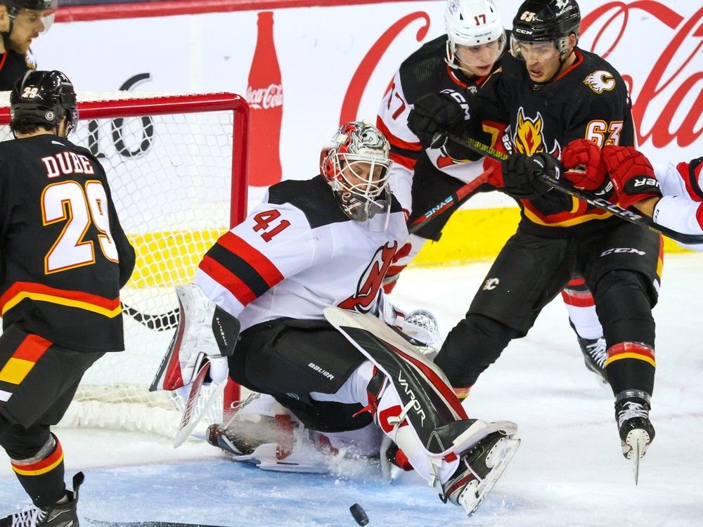 Calgary Flames forward Adam Ruzicka scrambles to reach a loose puck in front of New Jersey Devils goaltender Vitek Vanecek during NHL action in Calgary on Saturday, December 9, 2023. Gavin Young/Postmedia