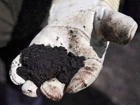 An oil worker holds raw oilsands near Fort McMurray, Alta., on July 9, 2008. Alberta university researchers are calling for an open public inquiry into a provincial program designed to ensure oilsands producers can pay to clean up after themselves.