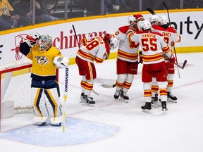 The Calgary Flames celebrate a goal by Yegor Sharangovich #17 as goaltender Juuse Saros #74 of the Nashville Predators drinks water during the third period at Bridgestone Arena