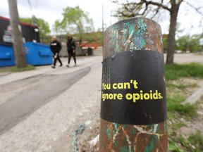Pedestrians walk past a sticker raising awareness about opioids in Edmonton.