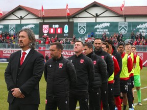 Cavalry FC staff Tommy Wheeldon Jr, Leon Hapgood and Nik Ledgerwood and reserves stand for the national anthem during CPL playoff soccer action