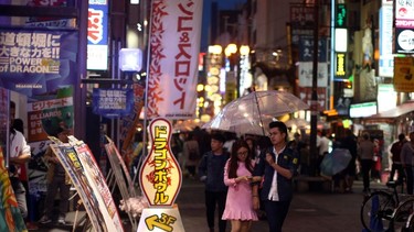 Visitors shelter from the rain under an umbrella on April 23, 2016 in the Dotonbori district of Osaka, Japan. The lively streets running along the Dontonbori Canal, are among the most iconic and popular tourist destinations in Osaka, the second largest city in Japan.