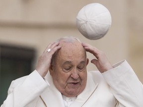 FILE - Pope Francis tries to catch his cap as wind blew it away while arriving for his weekly general audience in the St. Peter's Square at the Vatican, Wednesday, March 13, 2024.