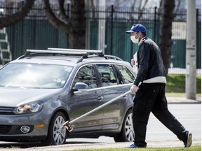 A man pictured during the pandemic on April 16, 2020, uses a pole with a cup on the end to ask for change from drivers on Toronto’s Lakeshore Blvd. (Postmedia News photo)