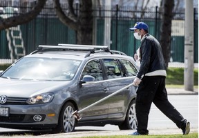 A man pictured during the pandemic on April 16, 2020, uses a pole with a cup on the end to ask for change from drivers on Toronto’s Lakeshore Blvd. (Postmedia News photo)