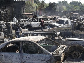 People look for salvageable pieces from burned cars at a mechanic shop that was set on fire during violence by armed gangs in Port-au-Prince, Haiti, Monday, March 25, 2024.